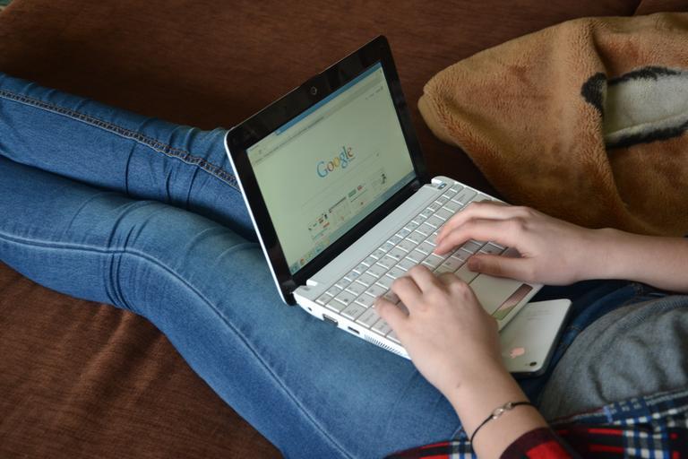 Žena má na kolenách notebook a zapnutý Google